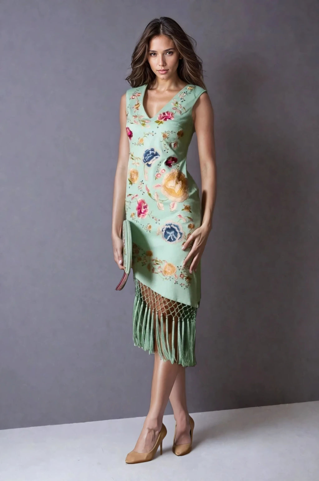 Model wearing a mint green sleeveless midi dress with colorful floral embroidery and long fringe hem, styled with tan heels and a green clutch.