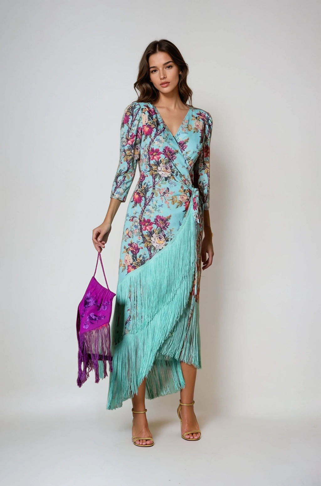 Model wearing aqua floral wrap dress with V-neckline and aqua fringe hem, holding a purple embroidered fringe bag