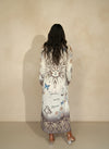 Back view of woman wearing long boho-inspired maxi dress with sun and moon design, blue butterflies, and script accents, styled with heeled boots.