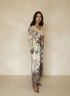 Side view of woman wearing printed floral and butterfly maxi dress with artistic portrait and ornate bohemian border, paired with brown boots.