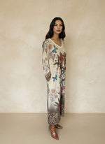 Side view of woman wearing printed floral and butterfly maxi dress with artistic portrait and ornate bohemian border, paired with brown boots.