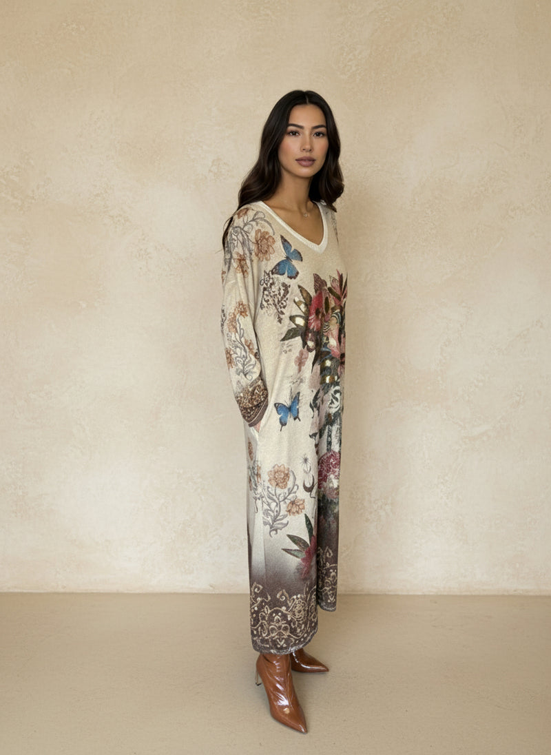 Side view of woman wearing printed floral and butterfly maxi dress with artistic portrait and ornate bohemian border, paired with brown boots.