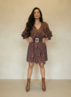 Model posing confidently in a brown polka-dot ruffle dress with layered skirt, V-neckline, and wide belt, styled with patent brown ankle boots.