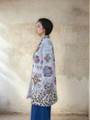Side profile of a woman modeling a gray printed long coat featuring vibrant Aztec-inspired motifs and animal print gradient hem, styled with blue wide-leg denim pants.