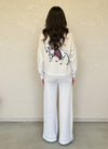 Back view of a cream knit sweater showcasing a detailed horse embroidery in red and white tones.