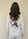 Close-up of horse embroidery on the back of a cream knit sweater with red saddle details.