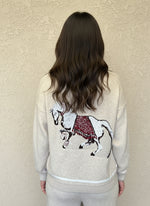 Close-up of horse embroidery on the back of a cream knit sweater with red saddle details.