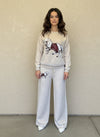 Woman wearing a cream knit lounge set with a white horse and red saddle motif, styled with white pointed heels.