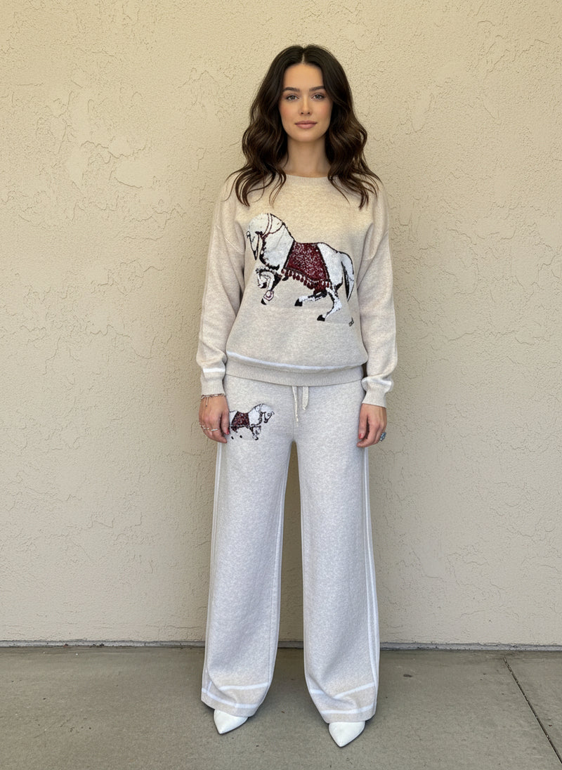 Woman wearing a cream knit lounge set with a white horse and red saddle motif, styled with white pointed heels.