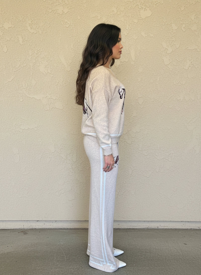 Side view of a woman wearing a cream knit set with a horse graphic, white trim, and wide-leg pants.