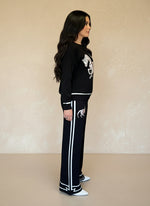 Side profile of woman in black knit horse-print sweater and matching pants with white stripes and trim.