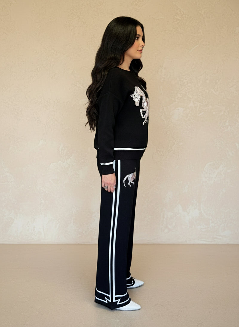 Side profile of woman in black knit horse-print sweater and matching pants with white stripes and trim.