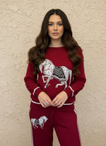 Woman in a deep-red knit matching set with a large white and black embroidered horse on the sweater and pants.