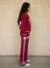 Side view of woman in red knit loungewear set with horse embroidery and white striped detailing on the pants.