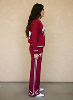 Side view of woman in red knit loungewear set with horse embroidery and white striped detailing on the pants.