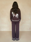 Back view of woman in a dark-brown knit loungewear set with a white embroidered horse motif on the sweater.
