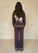 Back view of woman in a dark-brown knit loungewear set with a white embroidered horse motif on the sweater.