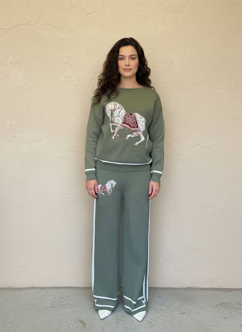 Woman wearing an olive-green knit loungewear set with a white embroidered horse motif and wide-leg pants with white side stripes.
