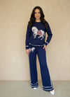 Woman wearing a navy knit lounge set featuring a white horse graphic on the sweater and pants, styled with white heels.