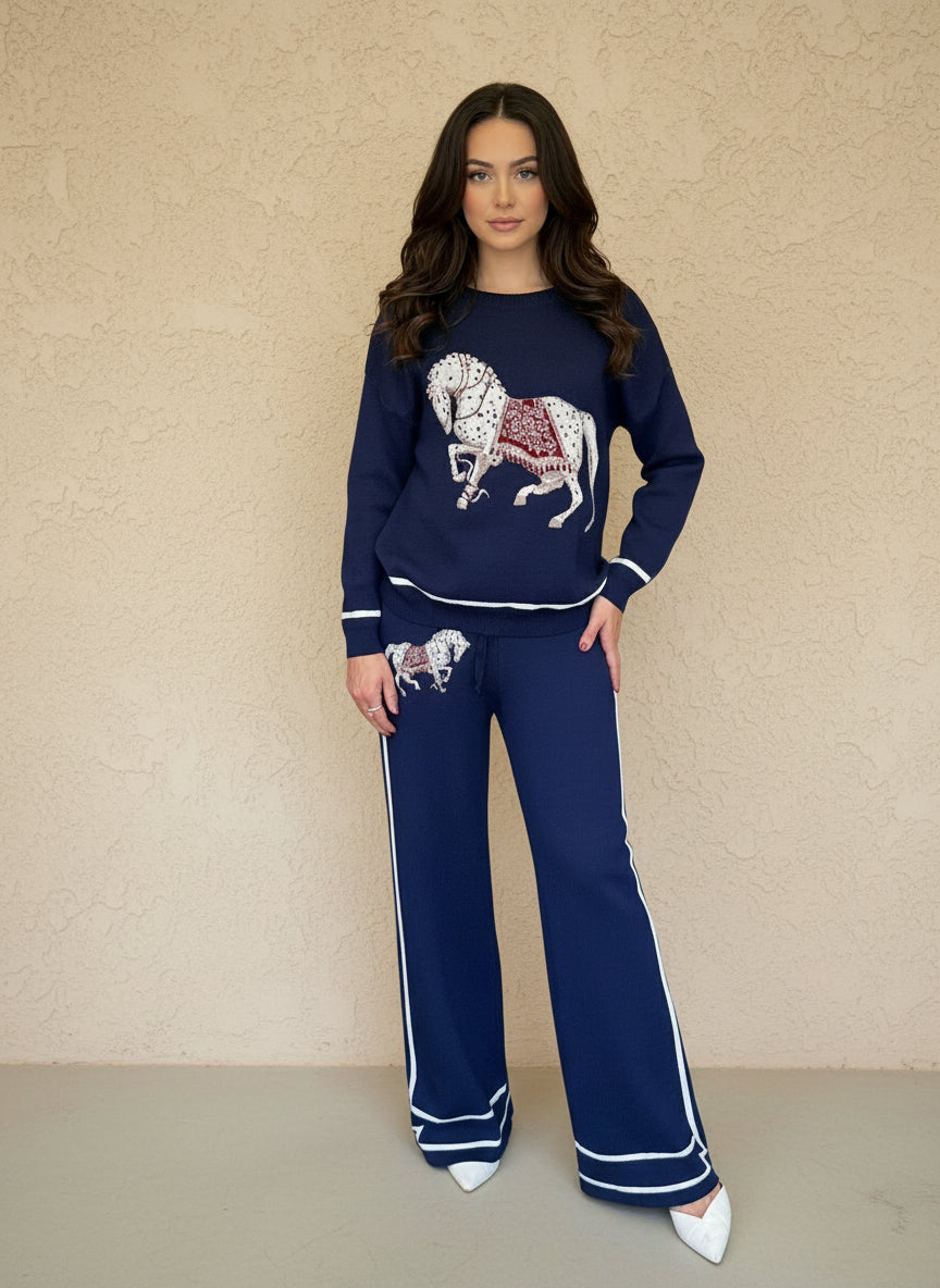 Woman wearing a navy knit lounge set featuring a white horse graphic on the sweater and pants, styled with white heels.