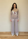 Woman modeling a taupe knit matching sweater and pants set decorated with horse embroidery and white accents.
