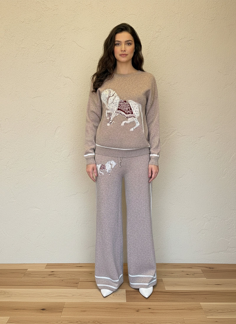 Woman modeling a taupe knit matching sweater and pants set decorated with horse embroidery and white accents.