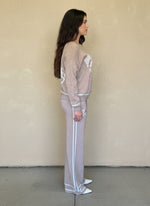 Side profile of a woman in a taupe knit loungewear set featuring horse motifs and white trim detailing.