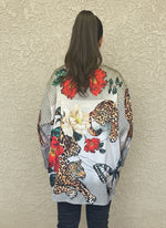Back view of satin blouse showcasing vivid red and cream floral prints with leopard and butterfly accents, styled with black jeans and wavy hair tied back.