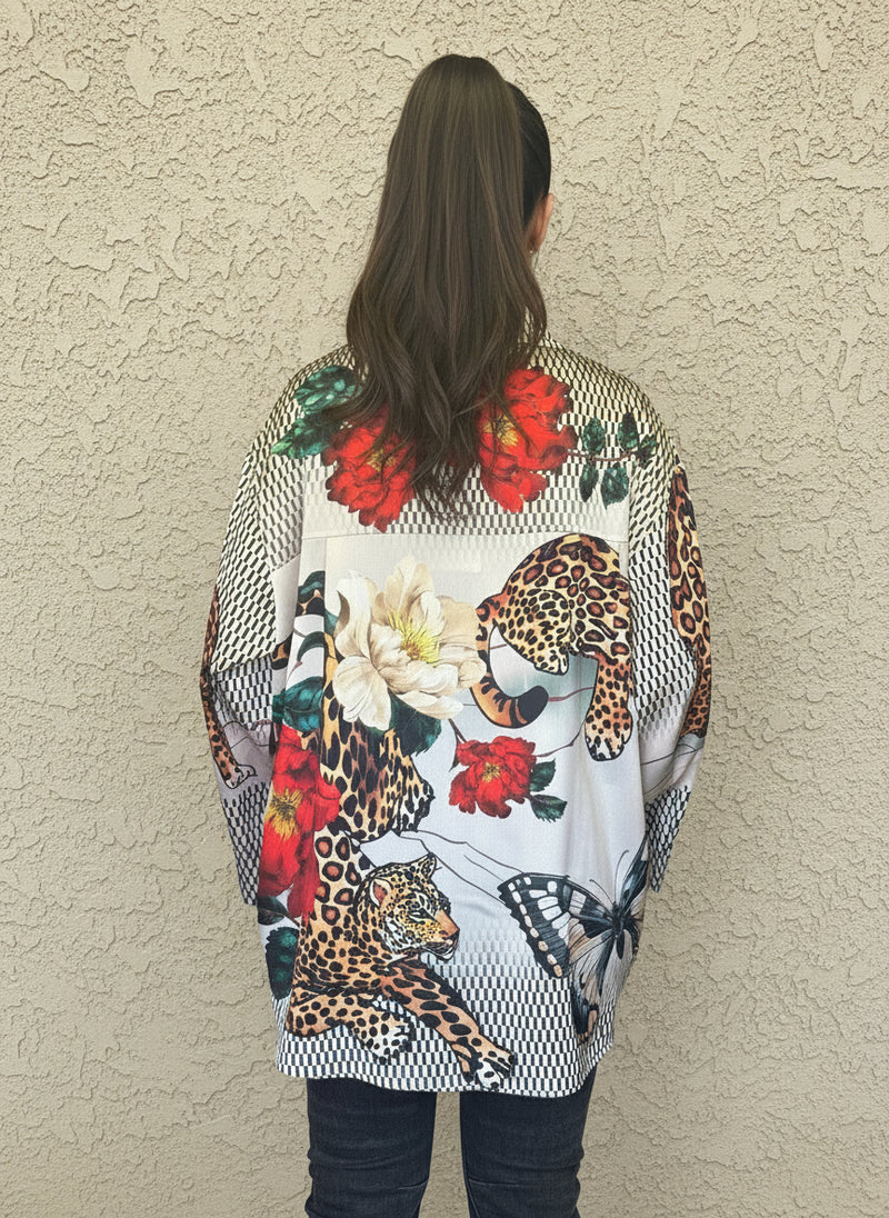 Back view of satin blouse showcasing vivid red and cream floral prints with leopard and butterfly accents, styled with black jeans and wavy hair tied back.