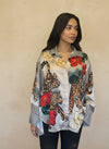 Model wearing a satin button-up blouse featuring bold leopard print, red and cream floral patterns, and a geometric black-and-white checkered design, paired with dark jeans.