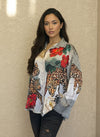 Model posing in a silky animal print blouse with bold leopard and red floral designs, paired with black jeans and minimal accessories, set against a beige wall.