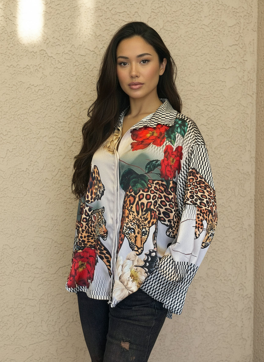 Model posing in a silky animal print blouse with bold leopard and red floral designs, paired with black jeans and minimal accessories, set against a beige wall.