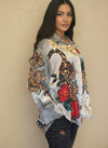 Side view of model in a satin leopard and floral blouse with red flowers and checkered details, styled with distressed black jeans against a neutral background.
