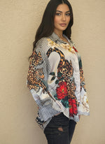 Side view of model in a satin leopard and floral blouse with red flowers and checkered details, styled with distressed black jeans against a neutral background.