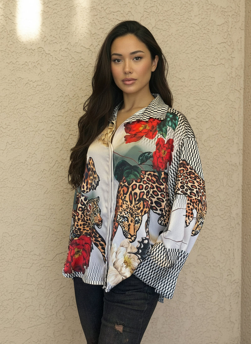 Model posing in a silky animal print blouse with bold leopard and red floral designs, paired with black jeans and minimal accessories, set against a beige wall.