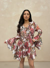 Close-up of woman in a romantic floral print dress with ruffle details, long bell sleeves, and a flared skirt, in shades of pink, red, and beige.