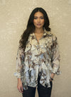 Woman modeling a cream and brown floral ruffled blouse with long sleeves, button-down front, and layered ruffles, paired with dark denim jeans against a neutral background.