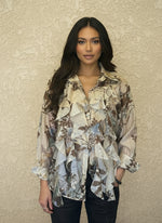 Woman modeling a cream and brown floral ruffled blouse with long sleeves, button-down front, and layered ruffles, paired with dark denim jeans against a neutral background.