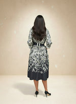 Back view of a woman in a belted black and white floral midi dress — elegant botanical print outfit with flowy skirt.