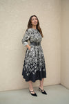 Model in a monochrome floral belted dress posing outdoors near a textured wall — stylish black and ivory floral midi dress.
