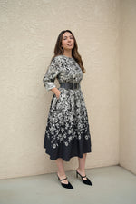 Model in a monochrome floral belted dress posing outdoors near a textured wall — stylish black and ivory floral midi dress.