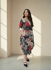 Model in a black and red floral print midi dress with a belted waist and rolled sleeves, posing in natural light near a cream-colored wall for a fall fashion look.