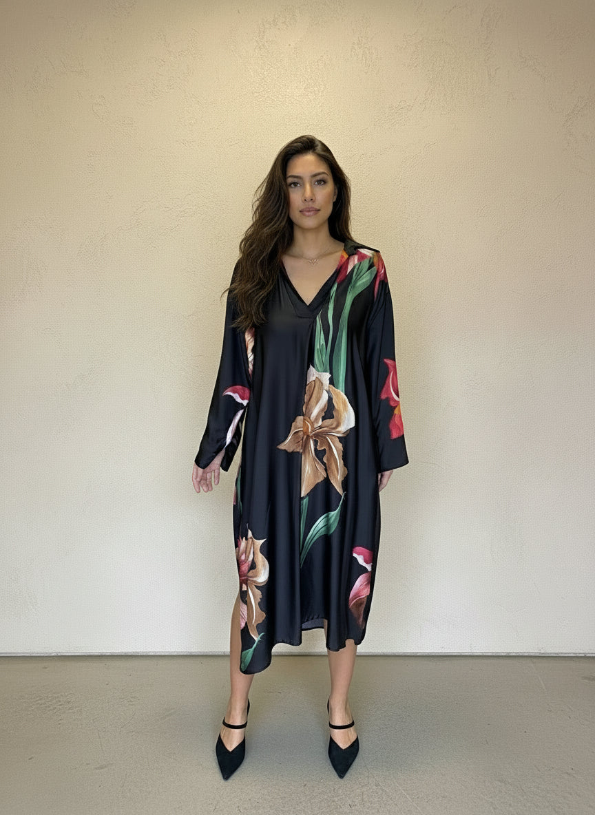 Stylish woman in black floral satin V-neck dress with long sleeves and pointed heels, posing front-facing against a neutral wall.
