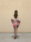 Model facing away wearing a brown plaid floral button-up shirt with red rose prints, paired with tan pants and brown ankle boots, standing against a beige wall.