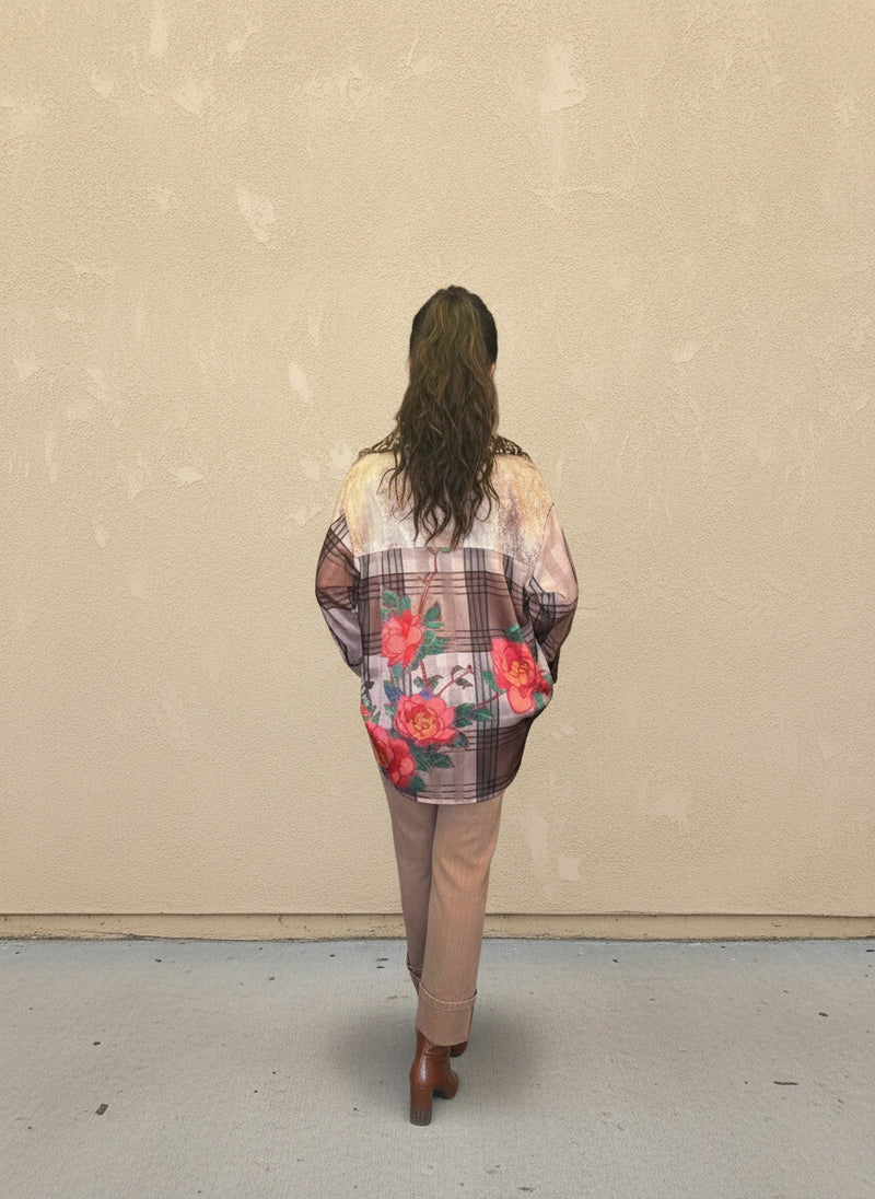 Model facing away wearing a brown plaid floral button-up shirt with red rose prints, paired with tan pants and brown ankle boots, standing against a beige wall.