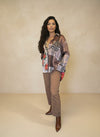 Model wearing a mixed-print plaid and floral blouse featuring leopard accents, styled with tan straight-leg pants and pointed brown boots in a neutral studio setting.