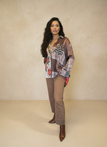 Model wearing a mixed-print plaid and floral blouse featuring leopard accents, styled with tan straight-leg pants and pointed brown boots in a neutral studio setting.