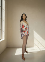 Side view of model in a brown plaid and floral shirt with red rose print, styled with beige slim-fit pants and brown pointed-toe boots in a softly lit studio.