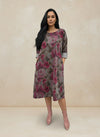 Front view of woman in a mauve and pink floral print A-line dress with pockets and rolled sleeves, paired with blush pink ankle boots against a neutral background