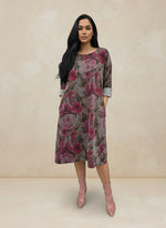 Front view of woman in a mauve and pink floral print A-line dress with pockets and rolled sleeves, paired with blush pink ankle boots against a neutral background